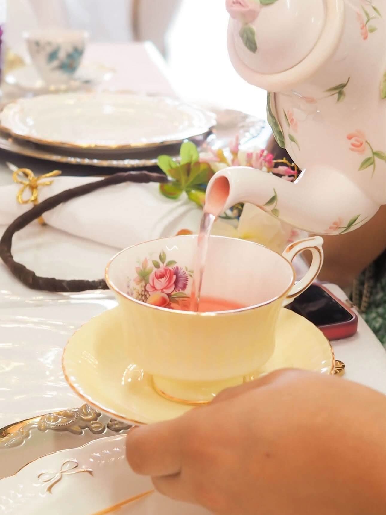 Tea being poured from a floral pot into a yellow flowered cup on a set table.